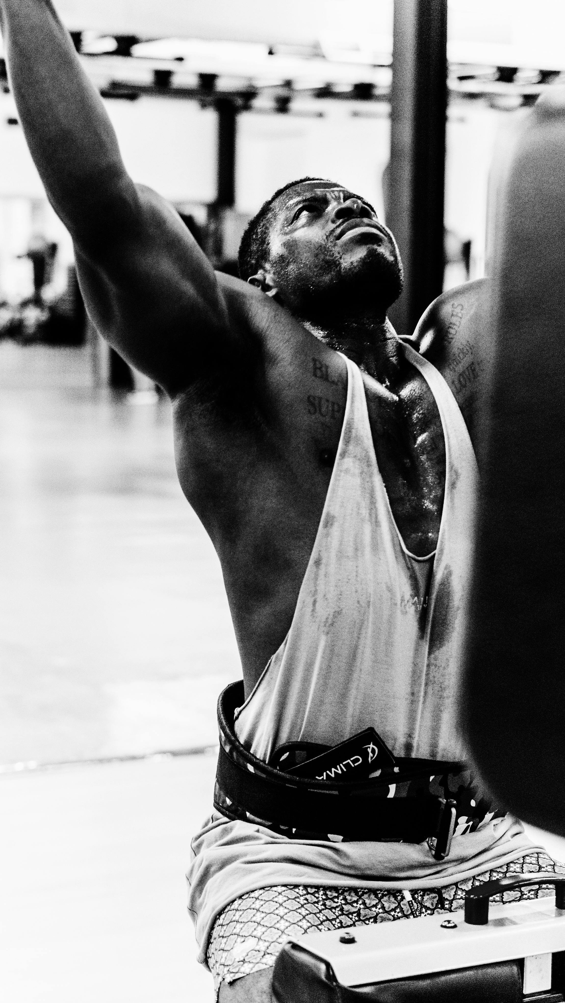 Black-and-white photo of a muscular man in a tank top lifting arms overhead at the gym, sweat on skin. Nutrition tips for building muscle can support his training.