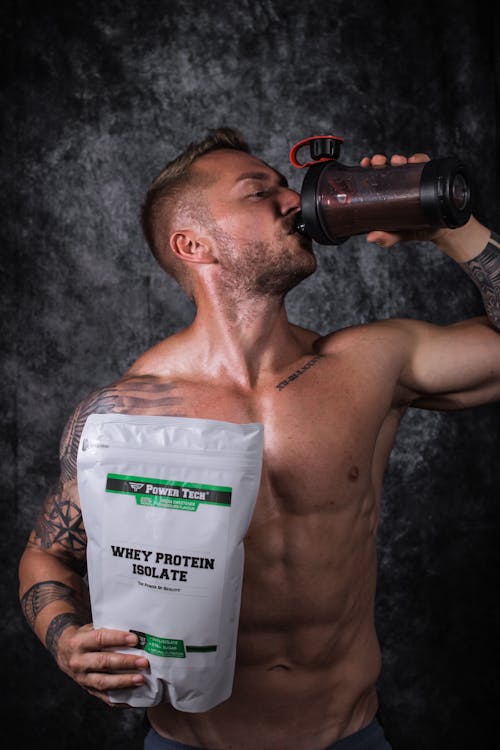 Athlete with visible abdominal muscles drinking a whey protein shake from a shaker bottle in a gym