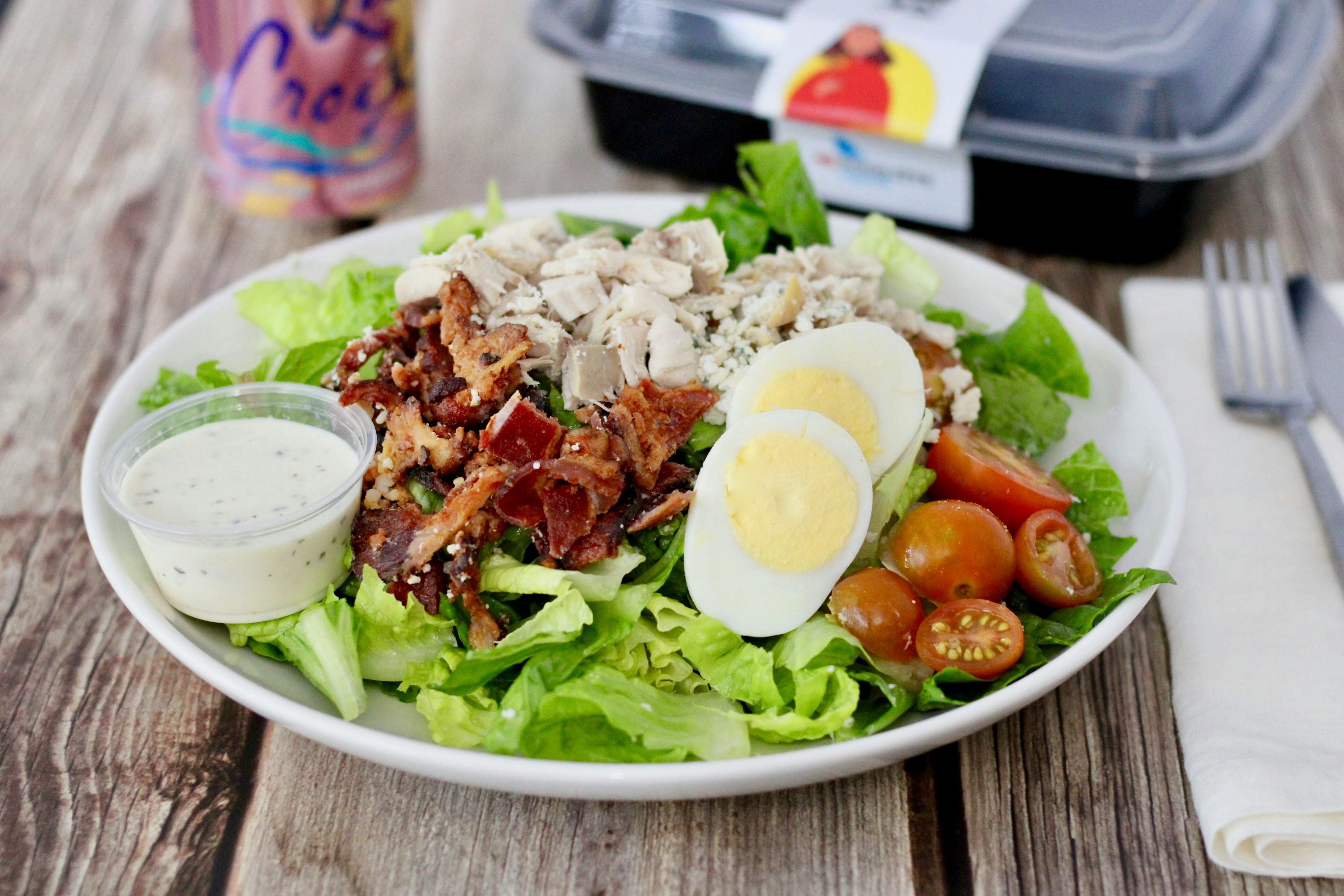 Bunter Salat mit Hähnchen, hartgekochten Eiern, Kirschtomaten und Speck, dazu cremiges Dressing in einer Schüssel. High protein rezepte abendessen.