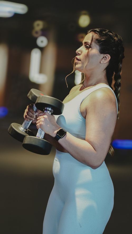 Coach en salle, femme tenant des haltères lors d’un entraînement, montrant un programme full body ou split adapté au niveau.