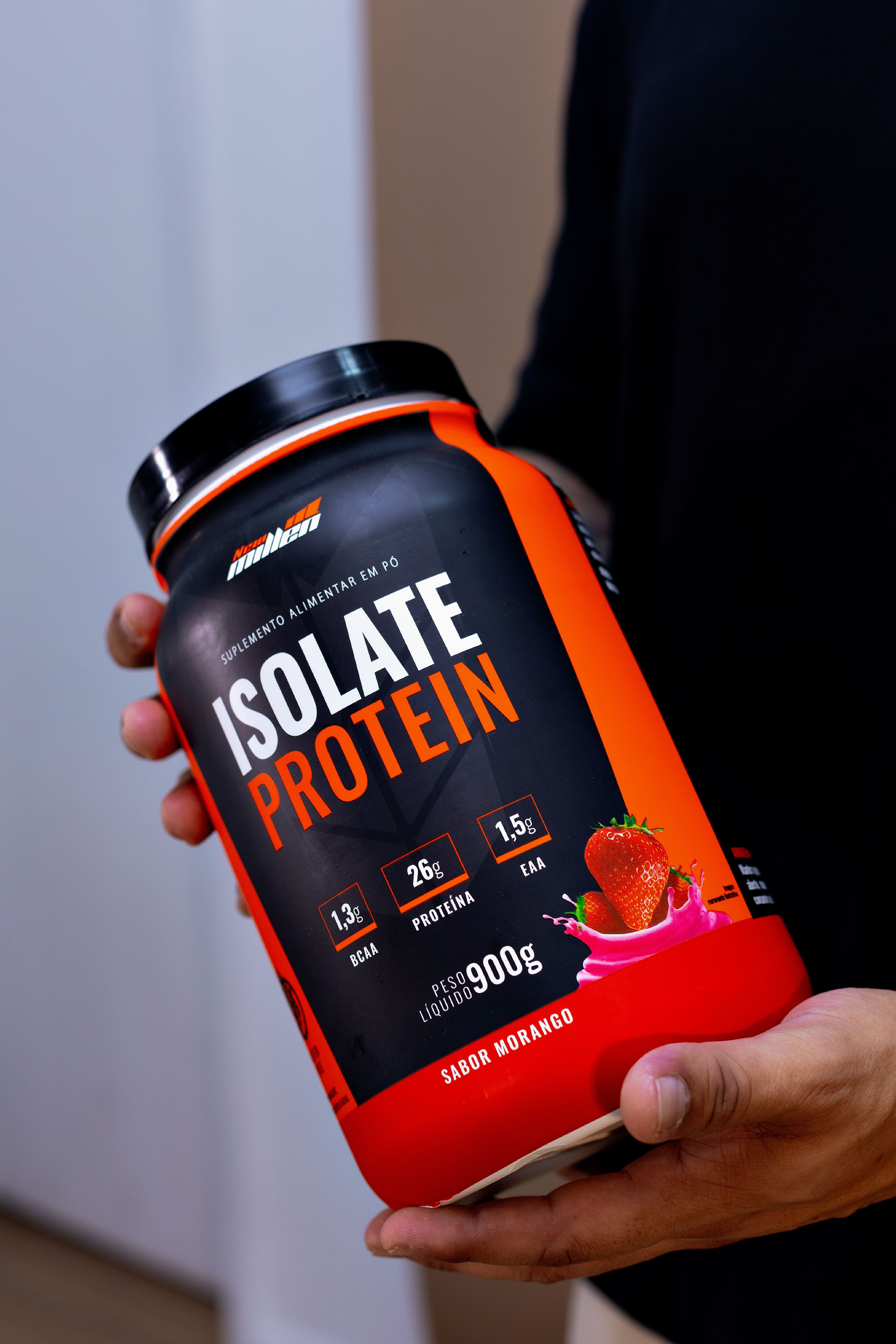 Container of Isolate Protein powder being held, with bold orange and white label showing strawberry imagery. How to use protein powder and creatine referenced.