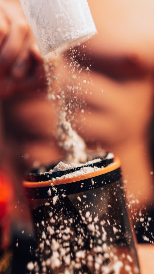 Scooping protein powder into a shaker, with powder dusting around the lid. protein powder for weight loss and muscle gain female blend.
